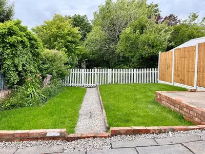 a backyard with a white fence and a grass yard at Cosy Bungalow & Peaceful Garden in Halsall