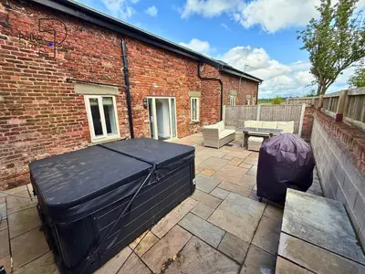a patio with two ottomans and a brick building at No 2 PolkaStays Ivy Farm Rosewood Cottage in Plumpton