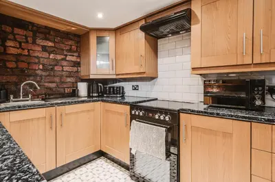 a kitchen with wooden cabinets and a brick wall at Liverpool Warehouse Flat - Sleeps 5, WiFi, Free On-Site Parking in Liverpool