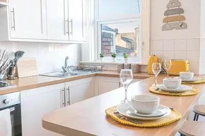 a kitchen with white cabinets and a table with wine glasses at Cozy & Modern Accommodation in Barrow-in-Furness in Barrow in Furness