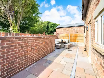 a brick wall next to a patio with a table at No 1 PolkaStays Ivy Farm Willow Cottage in Plumpton