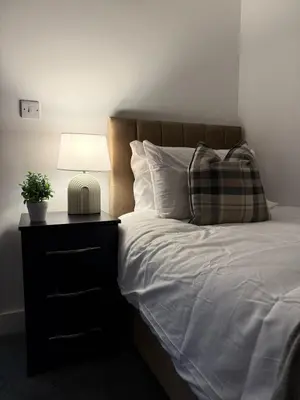 a bed with a nightstand with a lamp and a pillow at Comfortable and Modern Living house in St Helens in Saint Helens