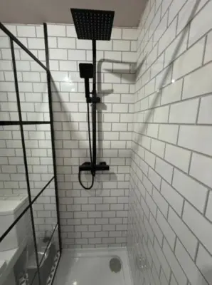 a white tiled bathroom with a shower with a light at The Wordsworth in Barrow in Furness