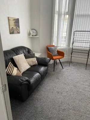 a living room with a black leather couch and a chair at The Beechwood in Blackpool