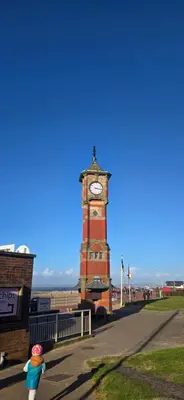 a clock tower with a child standing in front of it at Ocean Edge 13 in Heysham