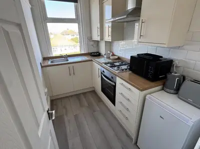 a small kitchen with white cabinets and a black microwave at Beach Apartments in Cleveleys