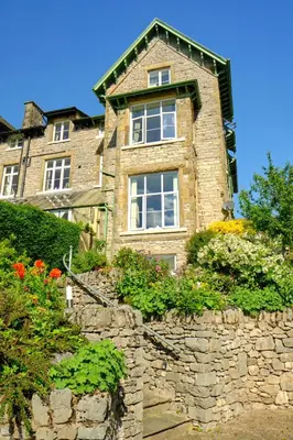 a stone house with a stone wall and flowers at Corner Beech House in Grange Over Sands