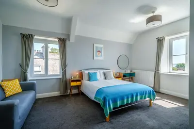 a bedroom with a bed and a couch and windows at Corner Beech House in Grange Over Sands