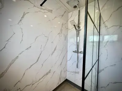 a bathroom with white marble walls and a shower at Keswick Hot Tub Family House in Lytham St Annes