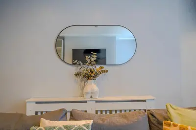 a mirror above a table with a vase with flowers on it at Stunning 1 Bedroom 4 Guest Flat by Anfield Stadium in Liverpool