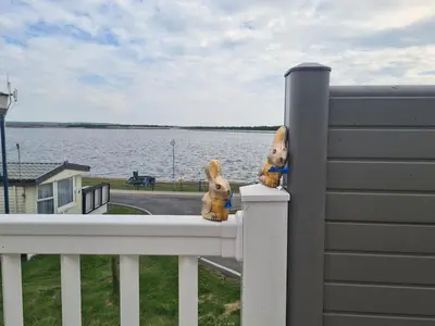 two stuffed animals are sitting on a fence overlooking the water at The Seaflower - With Lake Views in Millom