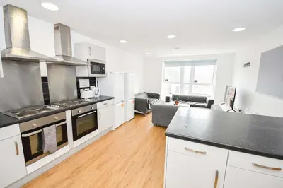 a kitchen with white cabinets and a living room at Convenient 8 Bedroom Apartment in Liverpool in Liverpool