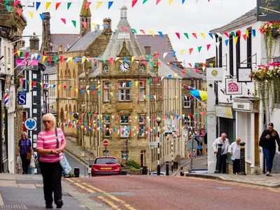 a woman walking down a city street with flags at Parson Castle View, Sleeps 6, Clitheroe Centre in Clitheroe