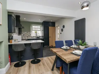 a kitchen and dining room with a wooden table and blue chairs at Holy Trinity Cottage in Millom