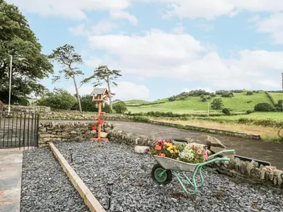 a wheelbarrow filled with flowers on a gravel road at Holy Trinity Cottage in Millom
