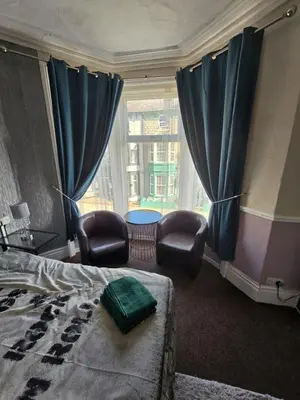 a bedroom with a bed and chairs and a window at The Lynbar Hotel in Blackpool