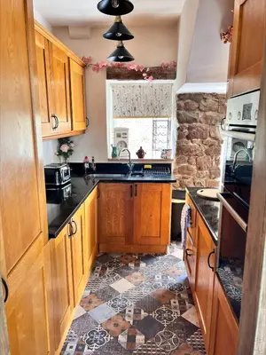 a kitchen with wooden cabinets and a tile floor at Nettle Cottage in Heysham