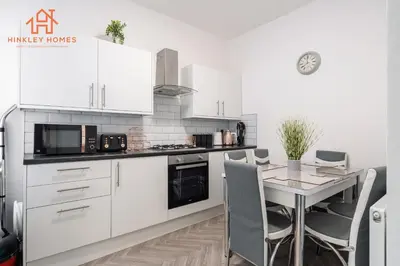a kitchen with white cabinets and a table with chairs at 9 Guests, 4 Bedrooms, Modern Comfort in Bootle in Litherland