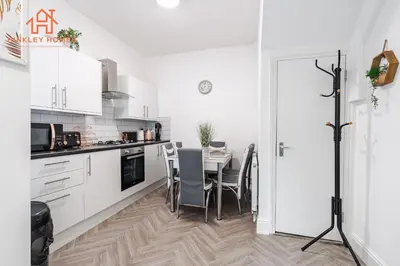 a white kitchen with a table and chairs at 9 Guests, 4 Bedrooms, Modern Comfort in Bootle in Litherland