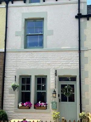 a white house with two windows and flowers at Historic 1600’s The Grocer’s Cottage in Heysham