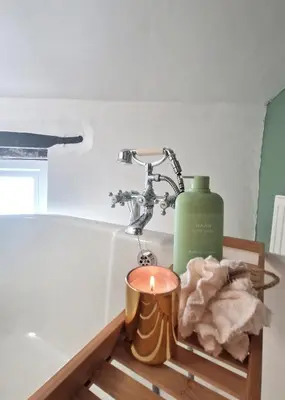 a candle sitting on a tray next to a bath tub at Historic 1629 May Cottage with Hot Tub in Heysham