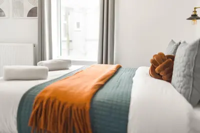 a bed with an orange blanket on it with a window at Aurum House Luxury Apartments in Blackpool