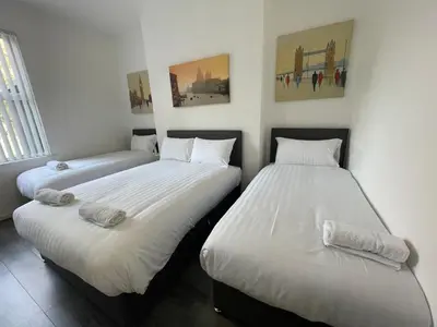 two beds in a room with white sheets at The LFC Red House - Spacious House With 5 Bedrooms, 2 Bathrooms, Street Parking And 1 Minute From The Stadium in Liverpool