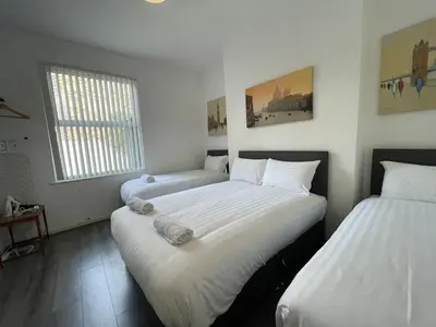 two beds in a room with white sheets at The LFC Red House - Spacious House With 5 Bedrooms, 2 Bathrooms, Street Parking And 1 Minute From The Stadium in Liverpool