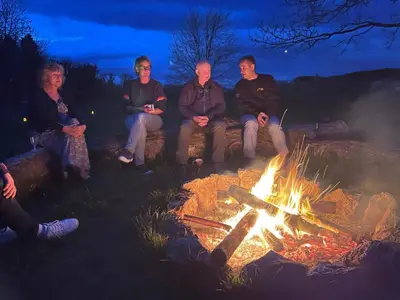 a group of people sitting around a fire at The Old Farmhouse, Yealand Redmayne, a characterful cottage in a rural setting in Beetham