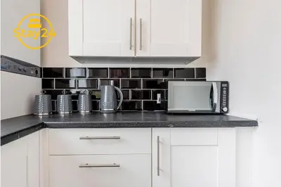 a kitchen with white cabinets and a black tile wall at Surrey Suite in Wallasey