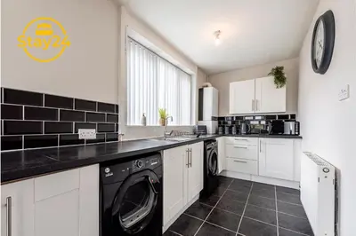 a kitchen with white cabinets and a washer and dryer at Surrey Suite in Wallasey