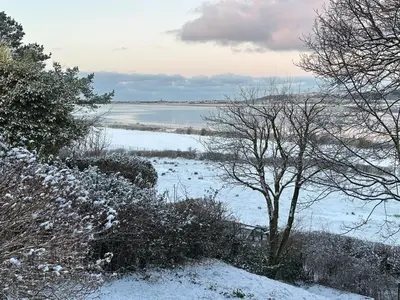 a snow covered field with a tree and a body of water at The Rookery Sandside - Luxury Coastal Home South Lake District and Beaches
