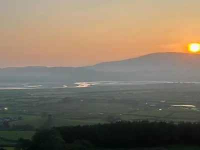 a sunset over a field with the sun in the sky at The Rookery Sandside - Luxury Coastal Home South Lake District and Beaches