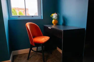 a orange chair sitting next to a black desk with a window at The Royal Alfred - Opposite Central Train Station in Saint Helens