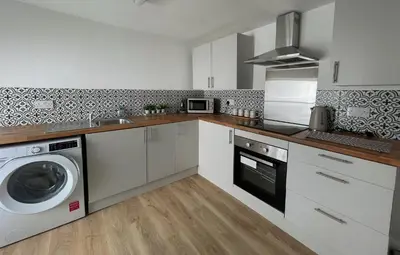 a kitchen with white cabinets and a washer and dryer at High Street Apartment in Garstang