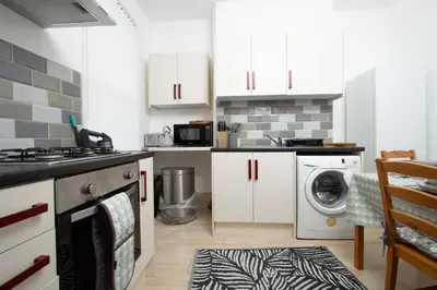 a kitchen with white cabinets and a washer and dryer at Cosy Studio Near Goodison & Anfield, Liverpool in Liverpool