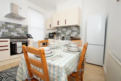 a kitchen with a table with chairs and a refrigerator at Cosy 2BR Flat Near Anfield & Goodison, Liverpool in Liverpool
