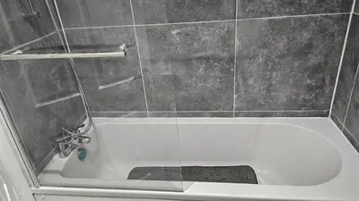 a bath tub with a shower with a glass door at A home away- 2 bedrooms in Saint Helens