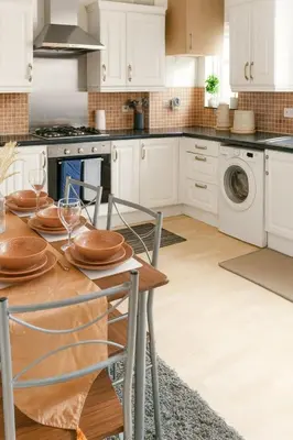 a kitchen with white cabinets and a table with wine glasses at Cosy Two-Bedroom House in Ormskirk in Pemberton