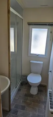 a bathroom with a toilet and a shower and a window at Lakeland leisure park sleeps up to 8 in Cark