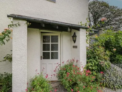 a white house with a white door and some flowers at The Laundrymaid's Cottage in Grange Over Sands