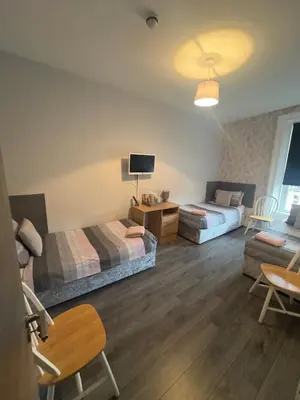 a room with two beds and a table and a tv at The Prince Alfred Rooms in Liverpool