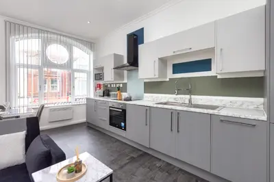 a large kitchen with white cabinets and a table at Charles Alexander Short Stay - South Pier Apartments in Blackpool