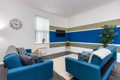 a living room with two blue couches and a tv at Charles Alexander Short Stay - South Pier Apartments in Blackpool