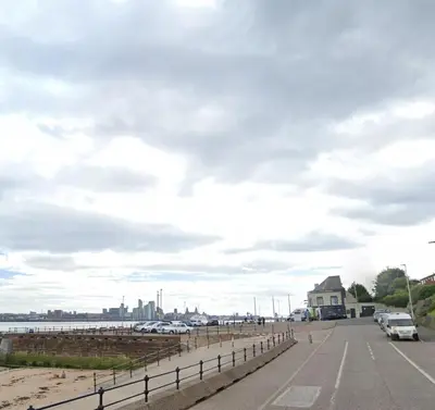 a parking lot next to the ocean with cars parked at Stylish and Bright 1 Bedroom Flat in Wallasey