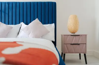a bed with a blue headboard next to a night stand at Mersey View 4 Bedroom by Liverpoollux Next To Everton Stadium in Liverpool