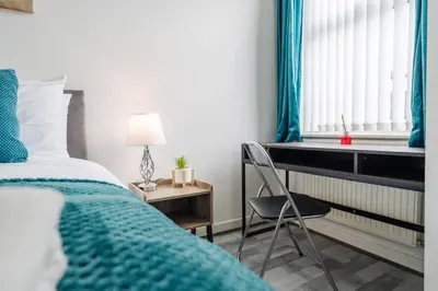 a bedroom with a bed and a chair next to a window at Newly Renovated 4BR House with lots of amenities in Liverpool