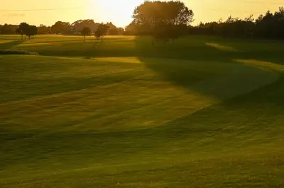 a green golf course with the sun setting in the background at Staining Luxury Lodges in Poulton le Fylde