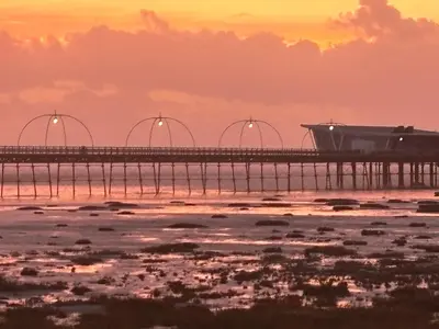 a pier over the water with a sunset in the background at Michaels Suite in Southport