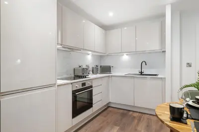 a white kitchen with white cabinets and a table at Luxury Waterfront Apartment - Liverpool City Centre - Sleeps 4 in Liverpool